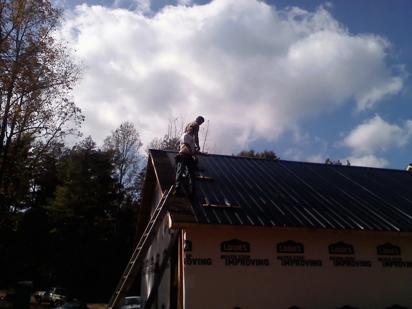 Roofer fastening dark metal panels high against a cloudy sky, from a Roof Inspection job in Santaquin