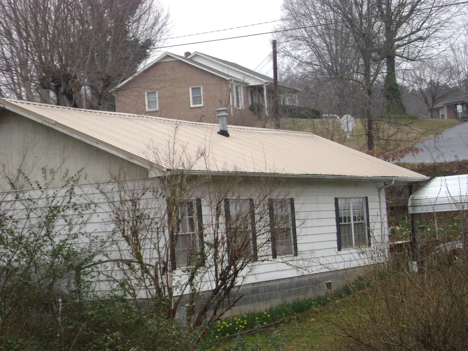 Tan metal roof on a white sided house set into a hillside — Commercial Roofing by Roofing Brothers in Santaquin